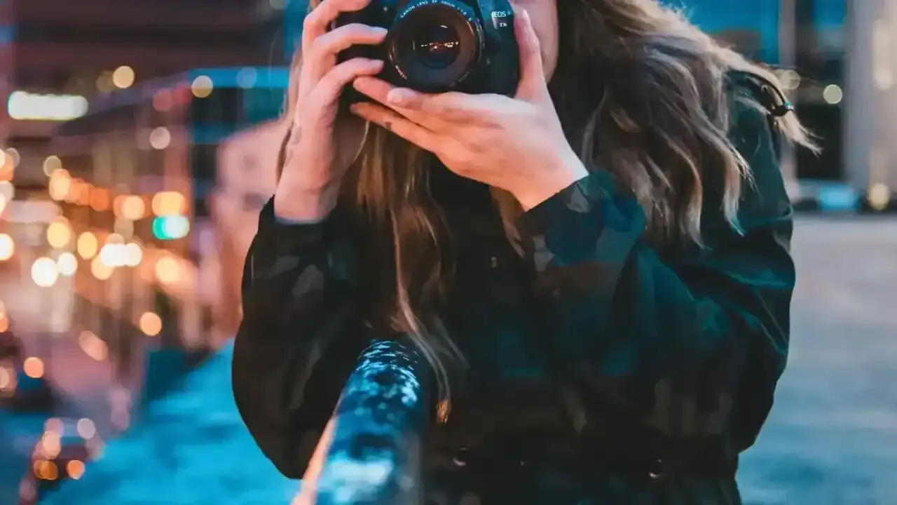 Fotógrafa grabando de noche con las luces de la ciudad al fondo